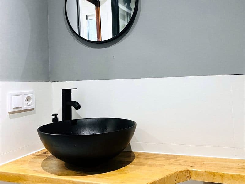 Grifería negra y lavabo sobre encimera de madera instalados en Ferrol